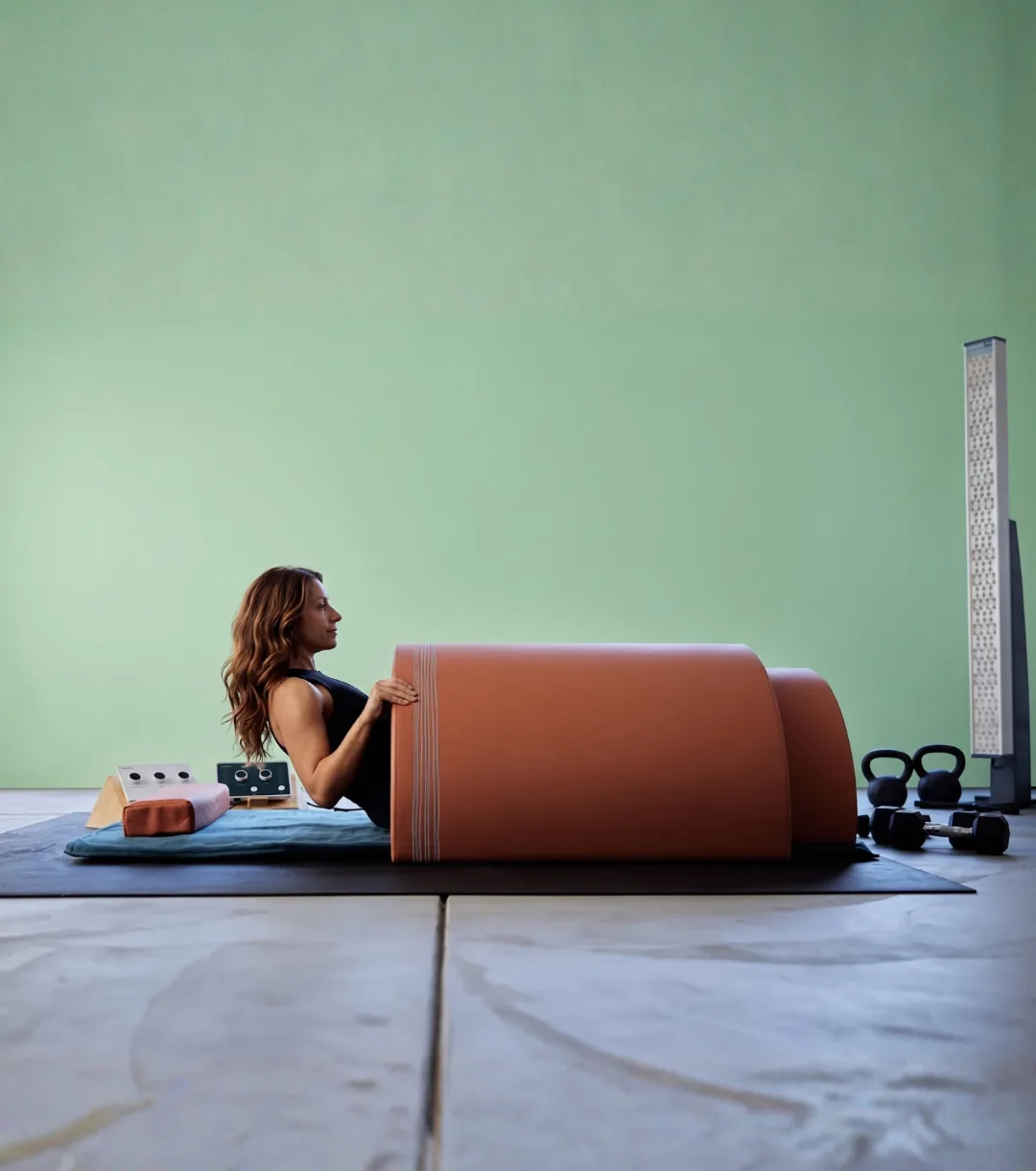 A person lying beneath a curved infrared sauna dome on a floor mat